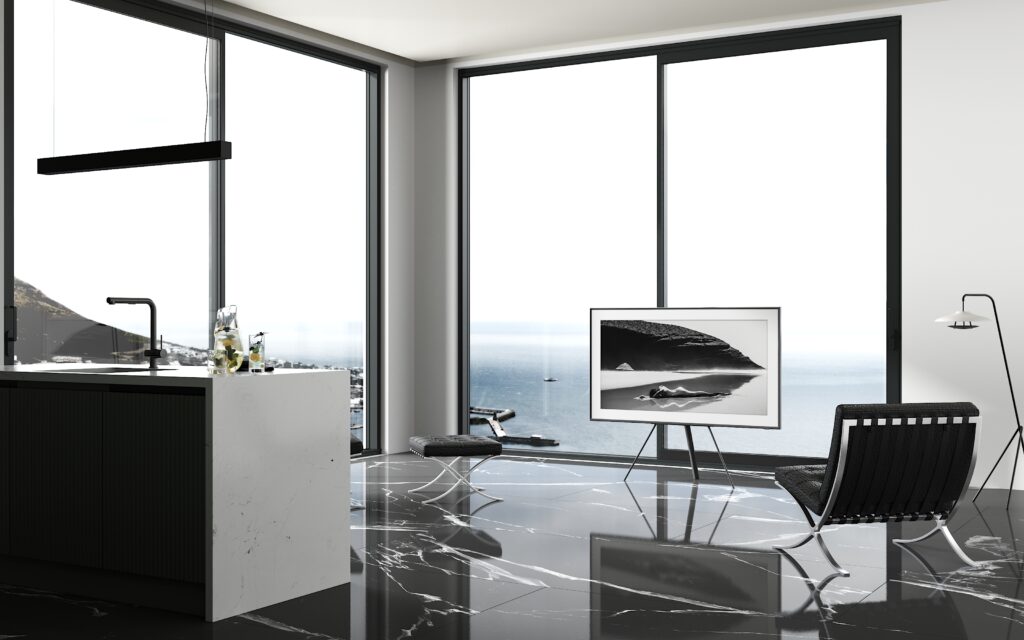 Nowoczesne mieszkanie z panoramicznymi oknami wychodzącymi na morze, wyposażone w minimalistyczne meble w kolorach czarno-białych. W pomieszczeniu znajdują się czarne fotele, kuchnia z wyspą oraz błyszcząca podłoga odbijająca światło.
