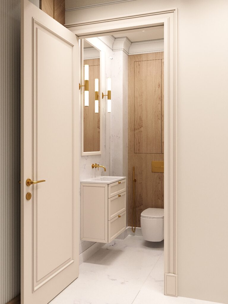 Elegancka łazienka w jasnych barwach z białą szafką podumywalkową ze złotymi uchwytami, drewnianymi elementami i wisząca muszlą klozetową. Widok przez otwarte białe drzwi pokazuje nowoczesne wnętrze z marmurowymi i drewnianymi akcentami oraz złotymi dodatkami.